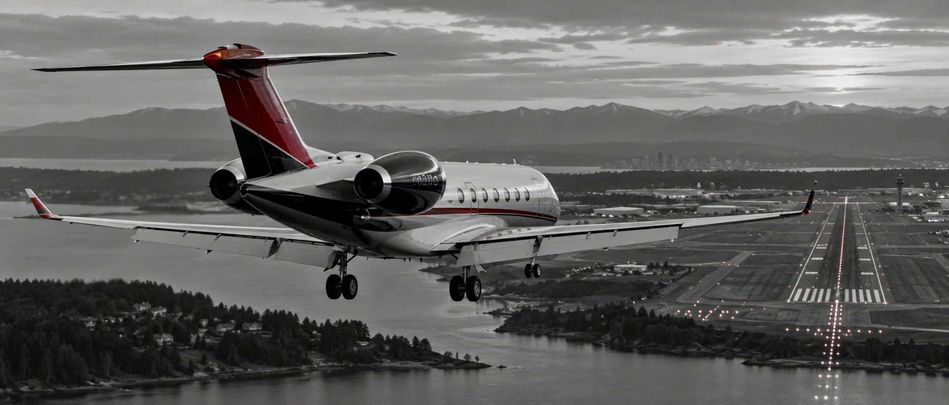Private jet on final approach to a runway at dusk, in black and white with crimson accents